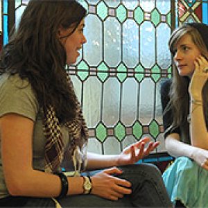 Chicas de diferentes nacionalidades conversando junto a una ventana.